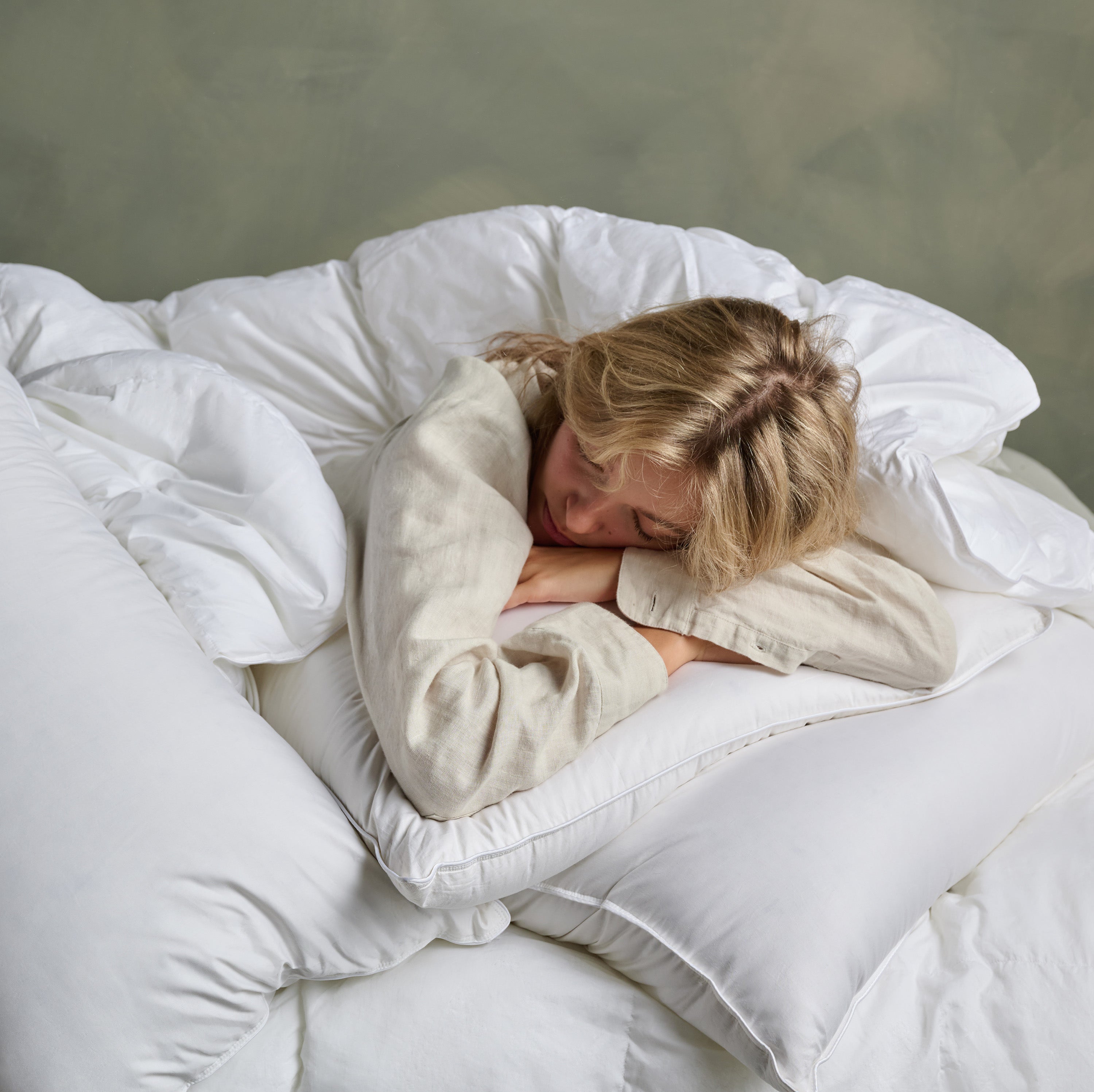 Person sleeping under a white comforter and pillow in a bedroom setting